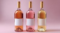 Three wine bottles with blank labels in different shades - rose, blush pink and white wine standing in row on pink background, mockup for wine industry.