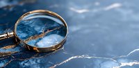 Magnifying glass on blue marble surface with gold veins. Elegant detective concept showing investigation and research against luxurious stone background.