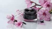 Black cosmetic cream jar with pink cherry blossom flowers on white background, luxury skincare product photography for beauty and wellness marketing.