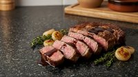 Sliced grilled beef steak with herbs and roasted garlic on dark stone surface. Perfect for restaurant menus, cooking blogs and culinary presentations.