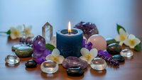 Healing crystals and gemstones arranged around burning candle with flowers for meditation, spiritual wellness, and holistic therapy practices.