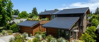 Modern eco-friendly house with solar panels on roof surrounded by lush green landscaping and trees under blue sky for sustainable living concepts.
