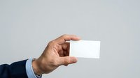 Man in business attire holding blank white card against neutral background, suitable for corporate branding, business card mockups, and professional presentations.