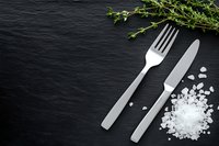 Fork and knife with fresh thyme and sea salt on dark slate stone background, top view. Elegant restaurant table setting concept.
