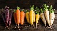 Fresh organic heirloom carrots in rainbow colors arranged on rustic wooden background for healthy cooking and farm-to-table cuisine concepts.