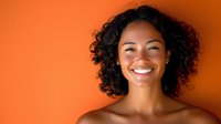 Young African American woman with curly hair smiling brightly against vibrant orange background, conveying happiness, confidence and positivity.