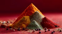 Colorful spice piles including turmeric, paprika, curry and chili powder arranged on dark red background with scattered peppercorns creating aromatic composition.
