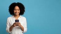 Happy African American woman with curly hair using smartphone on blue background for social media and communication concepts.