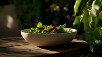 Fresh green salad with cherry tomatoes in white ceramic bowl on wooden table, dramatic natural lighting creates appetizing shadows and highlights.