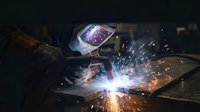 Professional welder in protective mask creating bright sparks while welding metal in industrial workshop with dramatic lighting and safety equipment.