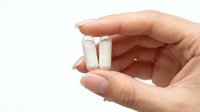 Hand holding two white capsules or pills against clean background for healthcare and pharmaceutical concepts.