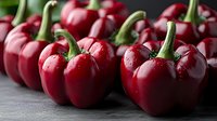 Fresh red bell peppers with water drops on dark background, macro shot showing texture and glossy surface. Organic produce for healthy cooking.