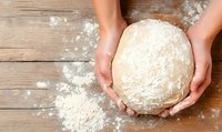 Female hands kneading fresh yeast dough on rustic wooden table with scattered flour, captured from above showing baking preparation process.