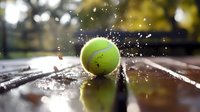 Tennis ball bouncing on wet court surface with water splashing around it, creating dynamic sports action scene in outdoor setting.