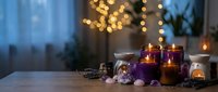 Cozy spa wellness setup with purple candles, essential oils and dried lavender on wooden table. Relaxing aromatherapy scene with warm bokeh lights background.