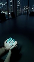 Hands holding glowing blue geometric crystal in dark office with city lights background for technology and innovation concepts.