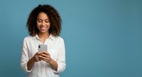 Happy young African American woman with curly hair using smartphone on blue background for social media and communication concepts.