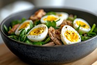 Fresh spinach salad with sliced hard-boiled eggs and walnuts in dark bowl. Healthy protein-rich meal with leafy greens and nuts for nutritious dining.