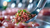 Fresh minced raw beef tartare garnished with chopped chives on metal spoon, close-up view against blurred restaurant background, gourmet appetizer.