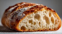 Freshly baked artisan sourdough bread with crispy crust and airy, open crumb structure showing characteristic holes in cross-section.