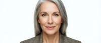 Mature woman with long gray hair and fair complexion wearing neutral blazer against white background, suitable for corporate, business, and professional portraits.