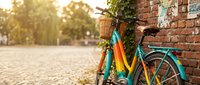 Colorful vintage bicycle leaning against brick wall with ivy in sunny urban setting, ideal for lifestyle, travel, and cycling content.
