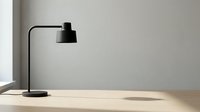 Modern black desk lamp with curved arm on wooden table against neutral wall, suitable for office and home workspace design projects.