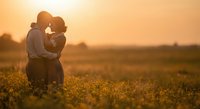 Romantic couple embracing in golden sunflower field at sunset, silhouetted against warm orange sky creating intimate moment for wedding and love concepts.