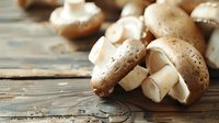 Fresh brown champignon mushrooms scattered on rustic wooden table, close-up view with selective focus showing natural texture and earthy tones.