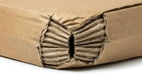 Damaged cardboard box corner showing corrugated layers and torn brown packaging material on white background isolated for shipping concepts.