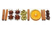 Aromatic spices and dried orange slice arranged in row on white background. Cinnamon sticks, star anise, cardamom pods, cloves for cooking and baking.