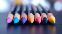 Vibrant colored pencils arranged in row on dark surface with soft bokeh background, showcasing rainbow spectrum of artistic tools for drawing and creative projects.