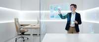 Young male professional in business casual attire presenting digital analytics charts on transparent screen in modern office workspace with minimalist design and natural lighting.