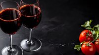 Two glasses of red wine with tomatoes and herbs on dark stone background, elegant composition for restaurant menu or wine tasting events.