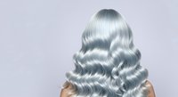 Young woman with long silver wavy hair styled in voluminous waves, viewed from behind against neutral background. Suitable for hair care, beauty, salon, and cosmetic product marketing.