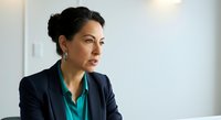 Confident middle-aged woman of Mediterranean ethnicity wearing professional navy blazer and teal blouse, looking thoughtfully to the side in modern office setting, suitable for business, leadership and corporate concepts.