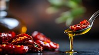 Sun dried tomatoes in olive oil dripping from spoon, close up view with dark moody background and selective focus, fresh Mediterranean ingredients.