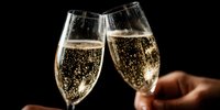 Two champagne flutes filled with sparkling wine clinking together in celebration toast against dark background with elegant lighting and bubbles.