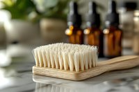 Natural wooden brush with white bristles on marble surface, amber glass bottles in background. Eco-friendly bathroom accessories for sustainable lifestyle.