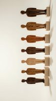 Collection of wooden figurines in varying wood tones and grain patterns mounted on wall-mounted shelves, displaying diverse carved human forms for home decor and artistic display.