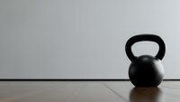 Black kettlebell on wooden floor against white wall in minimalist gym setting for fitness and strength training workouts.