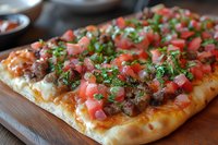 Fresh flatbread pizza topped with seasoned ground meat, diced tomatoes, onions and chopped herbs on wooden serving board, close up view of homemade meal.