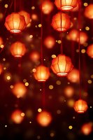 Glowing orange paper lanterns hanging against dark background with bokeh lights create magical festive atmosphere for celebration designs and holiday decor.