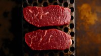 Raw marbled beef steaks on dark grilling surface with dramatic lighting, showcasing fresh meat texture and rich red color for food photography and culinary use.