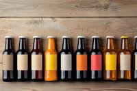 Craft beer bottles with blank labels in row on wooden background, showing variety of beer colors from light to dark amber and stout. Mockup for branding.