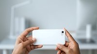 Hands holding white smartphone horizontally in modern office environment for mobile photography, app development, technology presentation, or digital content creation.