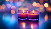 Two burning aromatic candles in glass jars against blurred bokeh lights background creating romantic atmosphere for spa, meditation or celebration.