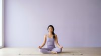 Woman in her 20s to 30s, South Asian ethnicity, practicing yoga in lotus position wearing lavender athletic wear on wooden floor against purple wall background.