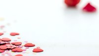 Red heart confetti scattered on white background with rose petals for romantic celebration and love themed designs.