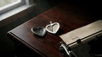 Open silver heart locket on wooden desk beside vintage typewriter with sorry note, evoking love, regret, and emotional storytelling.